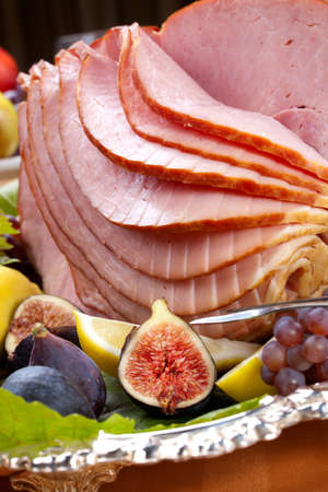 Glazed delicious whole baked honey sliced ham with figs, lemons and champagne grapes.の写真素材