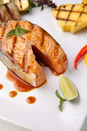 Delicious grilled Teriyaki salmon steak garnished with grilled pineapple, baby eggplants, zucchini and chilli pepper for healthy style dinner.の写真素材