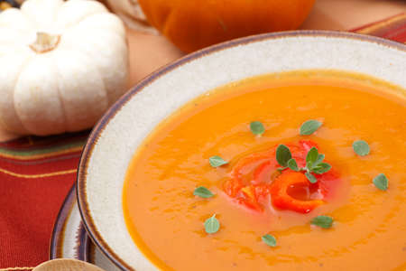 Closeup of a bowl of hot delicious spicy roasted bell pepper pumpkin soup garnished with fresh oreganoの写真素材