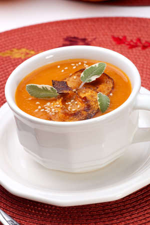 Closeup of a cup of hot delicious spicy roasted pumpkin soup with pumpkin crisps, sage and sesame seads.の写真素材