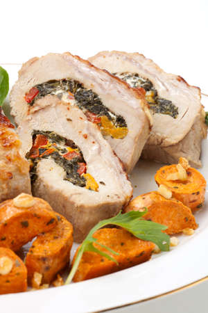 Feta-, spinach-, and bell pepper - stuffed pork tenderloin roulade garnished with sweet potato and green salad.の写真素材