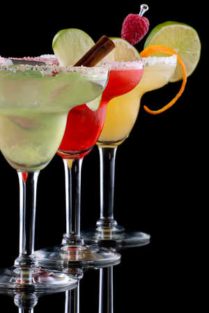Three Margaritas - apple, orange and raspberry - in chilled glasses over black background, garnished with slice of green apple, limes, orange twist, raspberry and cinnamon stick. Most popular cocktails series.の写真素材