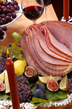 Glazed delicious whole baked honey sliced ham with figs, lemons and champagne grapes.の写真素材
