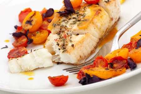 Pan fried halibut garnished with fennel seeds and spicy mustard sauce, served with fried cherry tomatoes salad with purple basilの写真素材
