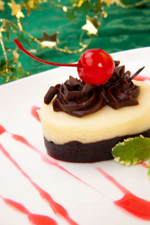 Closeup of delicious Chocolate Vanilla Cheesecake garnished with maraschino cherries and mint. Christmas ornament out of focus in backgroundの写真素材