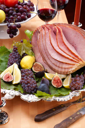 Glazed delicious whole baked honey sliced ham with figs, lemons and champagne grapes.の写真素材