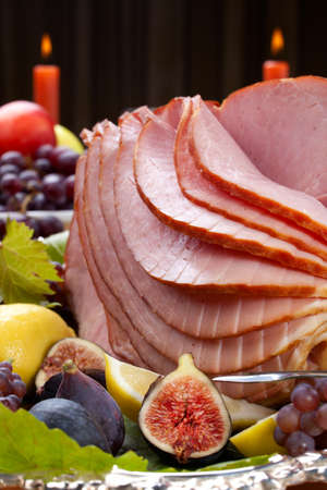 Glazed delicious whole baked honey sliced ham with figs, lemons and champagne grapes.の写真素材