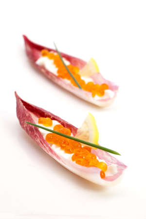 Closeup of red caviar on Creme Fraiche inside red endive leaf canape on white.の写真素材