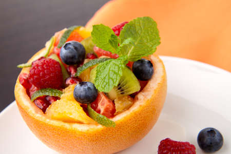 Serving of fresh fruit citrus berry salad in grapefruit peel. Kiwi, grapefruit, orange and pomegranate seeds.の写真素材