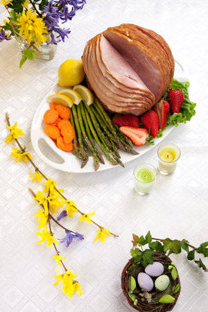 Festive glazed ham for Easter celebration dinner garnished with asparagus, carrots, strawberry, and lemon wedges.の写真素材