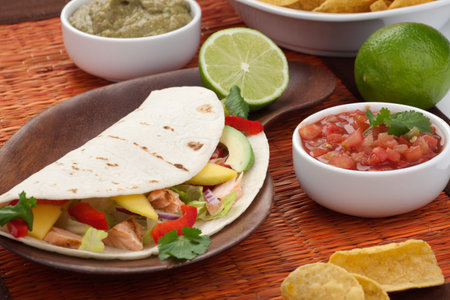 Closeup of grilled salmon fish tacos served with guacamole, fresh tomatoes salsa, and tortilla chips.の写真素材