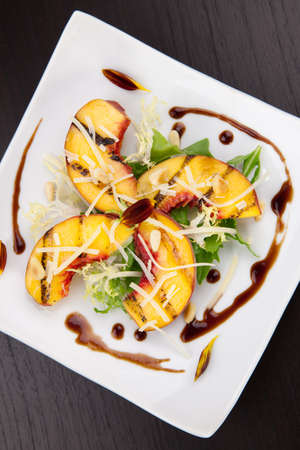 Closeup of grilled peaches salad with Parmesan cheese and roasted pine nuts. Balsamic vinegar sauce.の写真素材