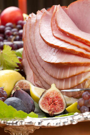 Glazed delicious whole baked honey sliced ham with figs, lemons and champagne grapes.の写真素材