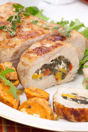 Feta-, spinach-, and bell pepper - stuffed pork tenderloin roulade garnished with sweet potato and green salad.の写真素材