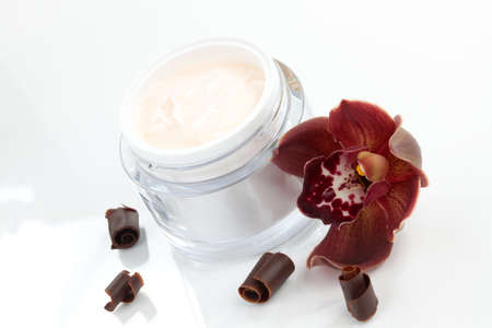 Closeup of jar of face cream and blooming chocolate colored Cymbidium orchid flowerの写真素材