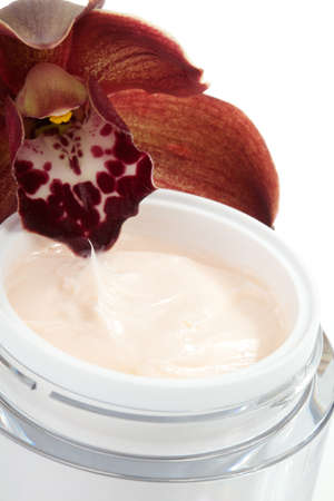 Closeup of jar of face cream and blooming chocolate colored Cymbidium orchid flowerの写真素材
