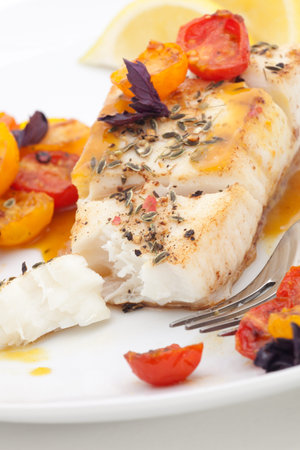 Pan fried halibut garnished with fennel seeds and spicy mustard sauce, served with fried cherry tomatoes salad with purple basilの写真素材