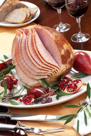 Dinning table set with glazed whole baked sliced ham, garnished with pomegranate, olives, and red pears.の写真素材