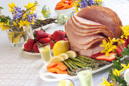 Festive glazed ham for Easter celebration dinner garnished with asparagus, carrots, strawberry, and lemon wedges.の写真素材