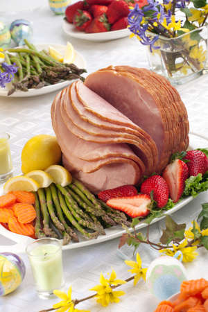 Festive glazed ham for Easter celebration dinner garnished with asparagus, carrots, strawberry, and lemon wedges.の写真素材