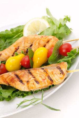 Closeup of grilled salmon on bamboo sticks and vegetable skewers with fresh tarragon and green saladの写真素材
