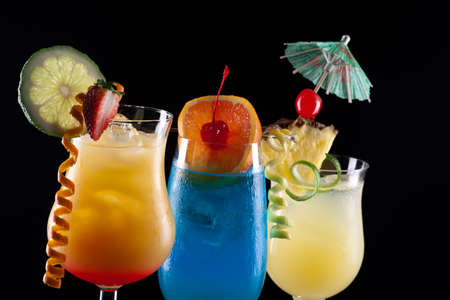 Tequila Sunrise, Blue Lagoon, and Bahama Mama cocktails over black background on reflection surface, garnished with strawberry, lime, pineapple flag, maraschino cherry, and lime twist  Most popular cocktails series の写真素材