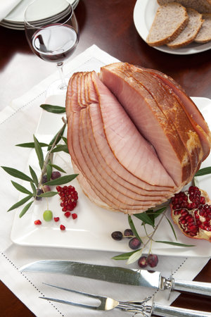 Closeup of plate with ham , bread and olives on dinning table set with glazed whole baked sliced...