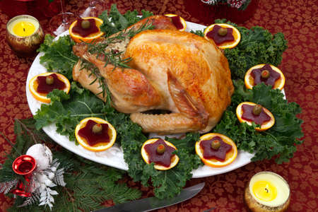 Christmas-decorated table with feast, gifts, roasted turkey, candles, champagne, and Christmas tree on back の写真素材