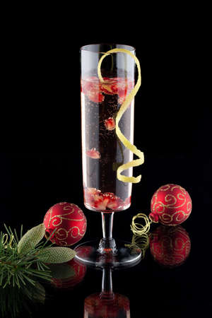 Closeup of glasses of pomegranate champagne cocktail, garnished with lemon twist, and Christmas ornaments on black background の写真素材