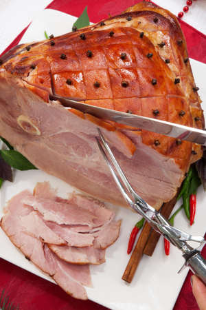 Carving roasted spiced ham on holiday dinning table, garnished with cloves, cinnamon sticks, hot chili pepper, and purple basil  Side dishes and Christmas ornaments around の写真素材
