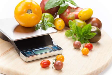 Digital kitchen scale on table surrounded with fresh tomatoes, and basil の写真素材