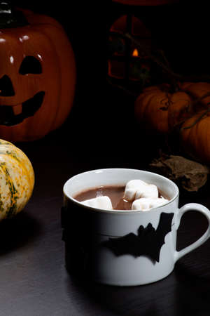 Cup of hot chocolate with ghost marshmallow, surrounded with pumpkins, candles, and Halloween decoration  Halloween drinks series の写真素材