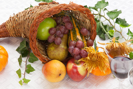 Horn of plenty full of fresh fruits - apples, pears, and grapes - on fall festival decorated table...