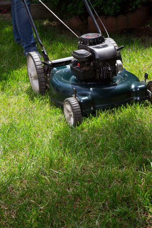 Woman is mowing her lawn with lawn mower in her back yard