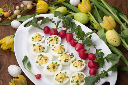 Plate of deviled eggs, fresh radish, Easter decoration eggs, and fresh spring blooming tulips 