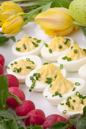 Plate of deviled eggs, fresh radish, Easter decoration eggs, and fresh spring blooming tulips 