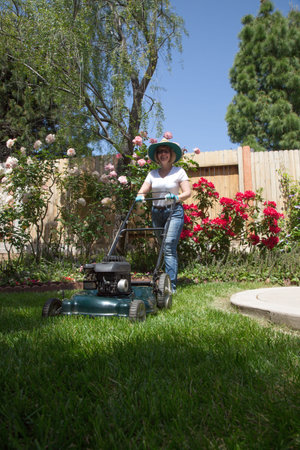 Woman is mowing her lawn with lawn mower in her back yard