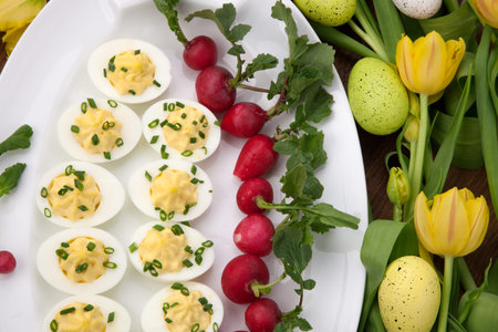 Plate of deviled eggs, fresh radish, Easter decoration eggs, and fresh spring blooming tulips 