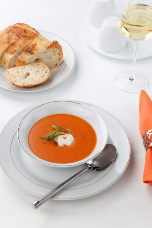 Bowl of lobster bisque garnished with slice of lobster tail, cream, and fresh tarragon  Fresh backed Italian bread and white wine の写真素材