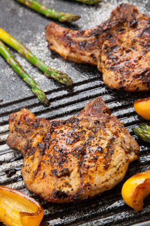 Juicy pork chops are grilled on griddle with asparagus and bell pepper  Backyard grilling for summer picnic の写真素材