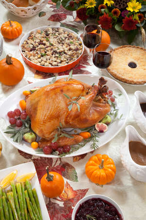 Roasted turkey on a server tray garnished with fresh figs, grape, kumquat, and herbs on fall harvest table  Red wine, side dishes, pie, and gravy  Decoraded with mini pumpkins, candels, and flowers の写真素材