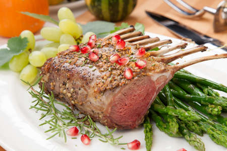 Herb crusted rack of lamb garnished with asparagus, green grapes, and pomegranates. Mini pumpkins and fresh fruits.の写真素材