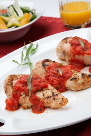 Grilled chicken breast with fresh tomato tarragon sauce, spinach - citrus salad, and orange juice.の写真素材
