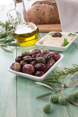 Greek style black olives, hummus, olive oil, and bread on a wooden tableの写真素材