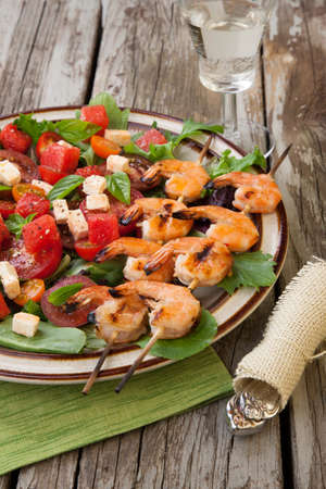 Plate of a grilled shrimp salad with feta cheese, tomatoes, and watermelon in a rustic setting.の写真素材