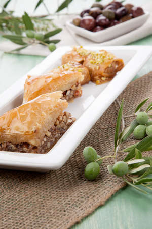 Mediterranean traditional pastries - Baklava - served with Greek style black olives on a wooden tableの写真素材