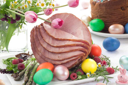 Whole baked honey sliced ham with fresh raspberry, asparagus, dyed Ester eggs, Easter cake, and cross buns. Spring flowers.の写真素材