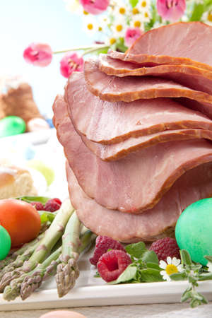 Whole baked honey sliced ham with fresh raspberry, asparagus, dyed Ester eggs, Easter cake, and cross buns. Spring flowers.の写真素材