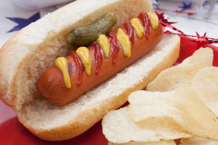 Hot dog, chips, and pickled cucumbers. Angel food fruit cakes and muffins on 4th of July in patriotic theme in background.の写真素材