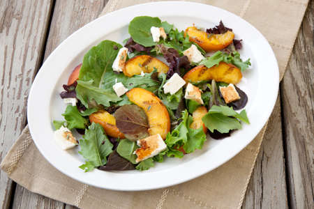 Plate of grilled peach and Mozzarella salad with mixed baby greens and balsamic vinegar in a rustic setting.の写真素材